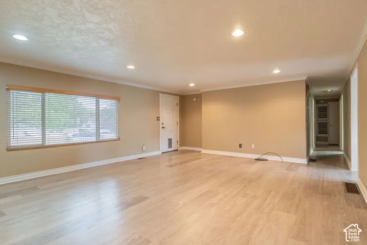 Recessed ceiling lighting, crown molding, wood-finish flooring, and a white entry door