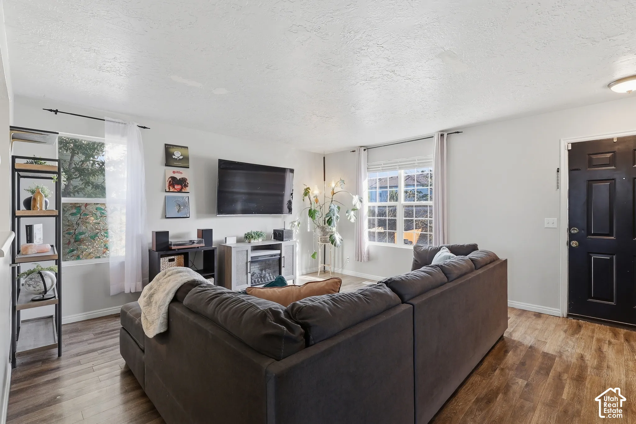 Spacious living area featuring wood-finish flooring, light gray walls, multiple windows, and a built-in electric fireplace