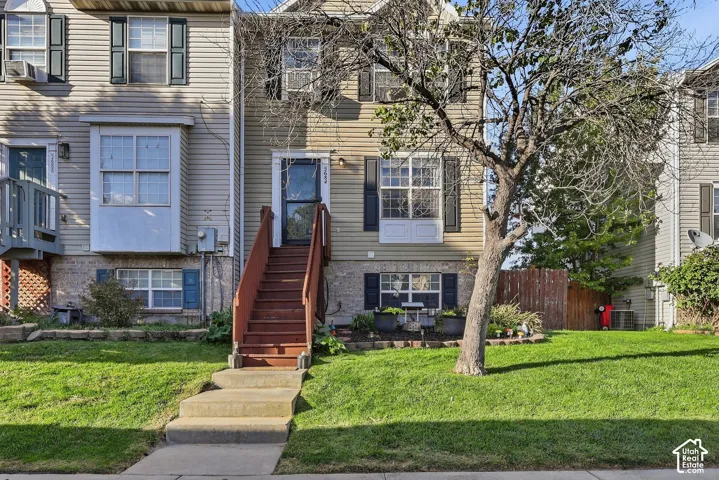 Exterior featuring a front lawn, sidewalk entry, wood-finish stairs, and a front door with storm door