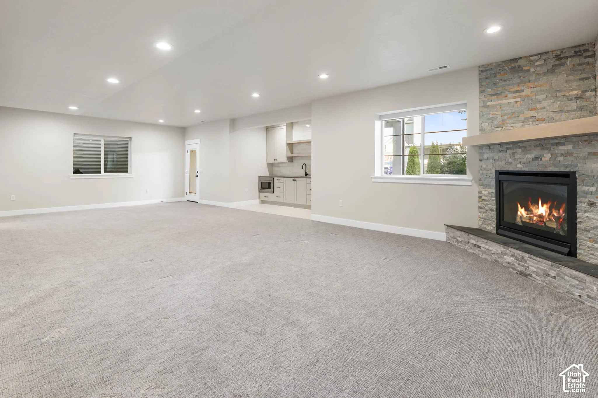 Spacious room featuring a stone-clad fireplace with a wood mantel, a built-in wet bar with cabinetry and sink, recessed lighting, and light-toned carpeting