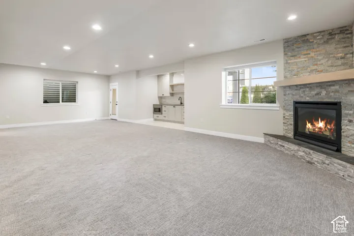 Spacious room featuring a stone-clad fireplace with a wood mantel, a built-in wet bar with cabinetry and sink, recessed lighting, and light-toned carpeting