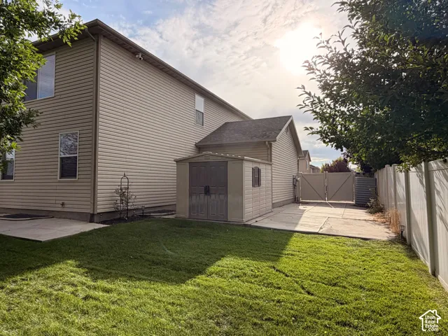 Manicured lawn, concrete patio, privacy fencing, side yard gate, and detached storage shed