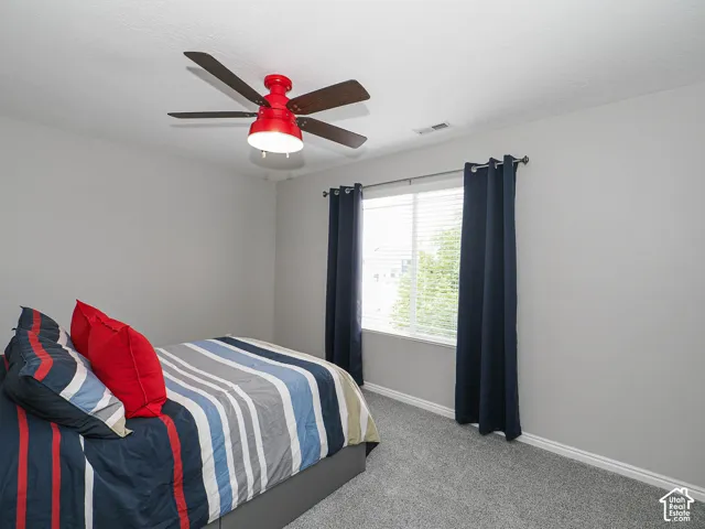 Bedroom featuring soft gray wall paint, light gray carpet flooring, and a window with white blinds and dark blue drapery.