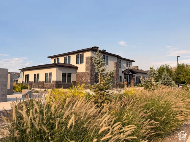 Stucco and stone exterior with prominent black-framed windows, a covered entry, and mature landscaping