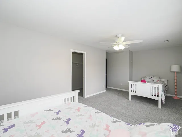 Expansive carpeted bedroom 3 with a Hunter ceiling fan light fixture and an open doorway revealing a large walk-in closet with shelving.