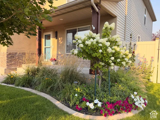 Front porch with a teal entry door, stone veneer accents, solid wood posts, and lush landscaping.