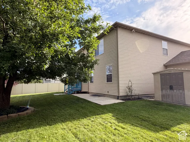 Expansive backyard featuring a manicured lawn, mature trees, concrete patio, and a utility shed