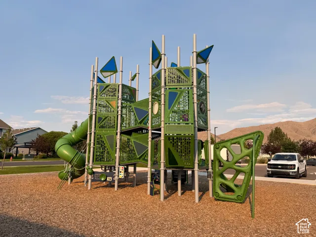 Playground structure featuring a tube slide, climbing wall, and elevated platforms, all set on a wood chip surface