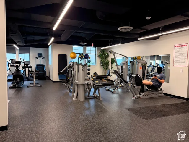 Fitness center featuring a variety of exercise equipment, rubber flooring, mirrored wall, and recessed linear lighting