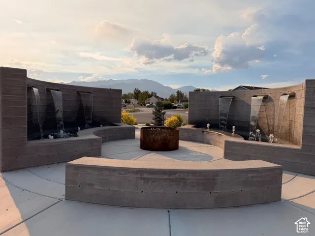 Curved concrete water feature with multiple cascades, integrated planters, and structured hardscaping, fire pit.