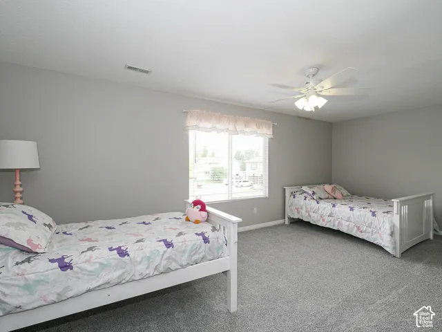 Newly carpeted bedroom 3 featuring a Hunter ceiling fan with integrated lighting, a large window with custom blinds, new light gray wall paint.