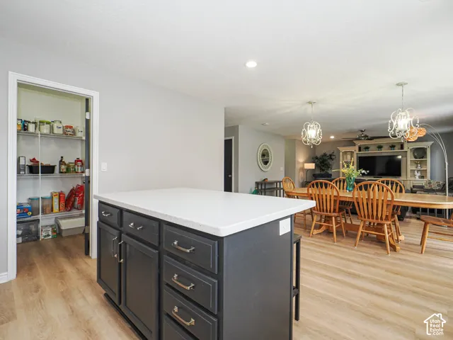 Kitchen island with white countertop and dark cabinetry, wood-finish flooring, and recessed lighting