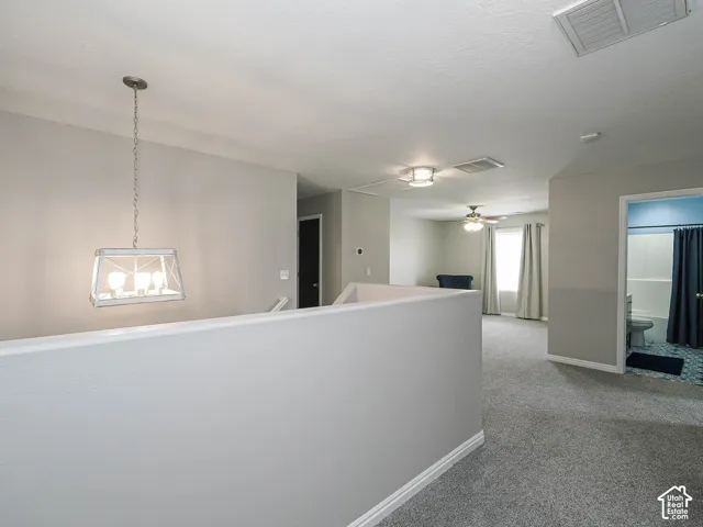 Carpeted loft area featuring a modern chandelier, ceiling fan, and window with curtains.