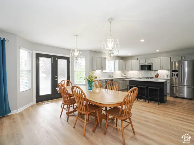 Open-concept kitchen and dining area featuring light wood-finish flooring, custom lighting, and french doors with built in blinds.