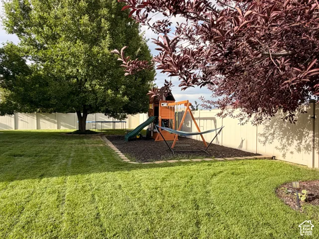 Expansive backyard featuring a manicured lawn, established trees, a privacy fence, and an included swingset.
