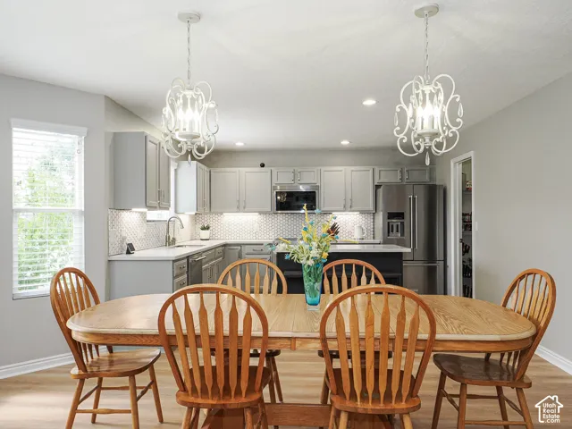 Open-concept kitchen and dining area featuring light gray cabinetry, brushed nickel hardware, new Corian countertops with white hexagonal tile backsplash, stainless steel appliances, custom lighting, recessed led canned lighting, and LVP wood-finish floor