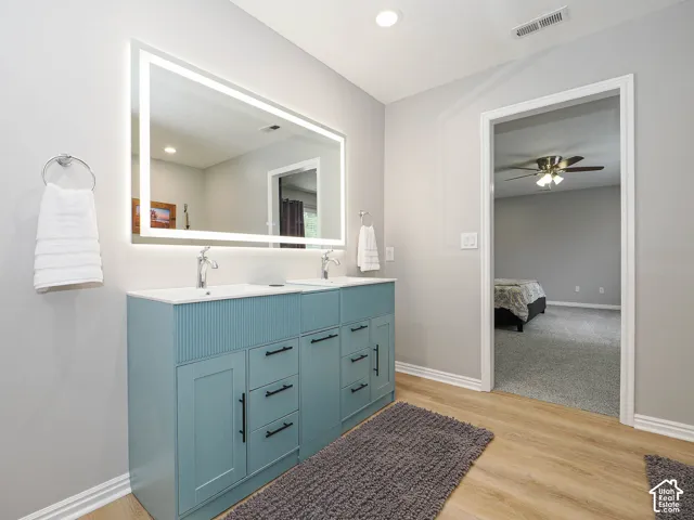 Modern bathroom vanity featuring dual sinks, a large backlit mirror, and light wood-finish flooring.