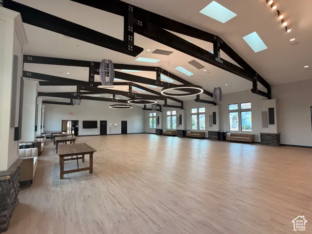 Clubhouse event space with vaulted ceiling with exposed wood beams, multiple skylights, wood-finish flooring, and recessed lighting