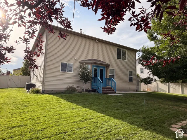 Siding exterior with multiple windows, a rear deck with blue railings, and a large grassy yard featuring a privacy fence