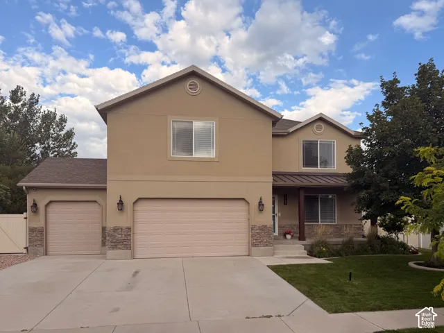 Stucco exterior with stone accents, three-car garage, covered entry, and manicured front lawn.