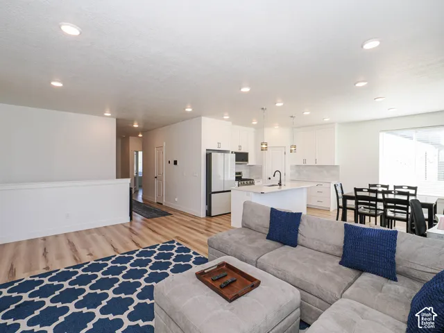 Open-concept living area with wood-finish flooring, recessed lighting, and a white kitchen featuring a large island, stainless steel appliances, and a tile backsplash