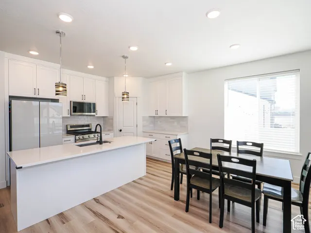 White shaker cabinetry, recessed lighting, wood-finish flooring, white solid surface countertops, and stainless steel appliances