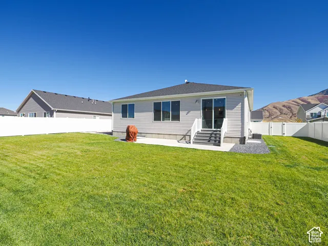 Expansive green lawn, white perimeter fencing, exterior patio space, mountain backdrop, and light-toned siding