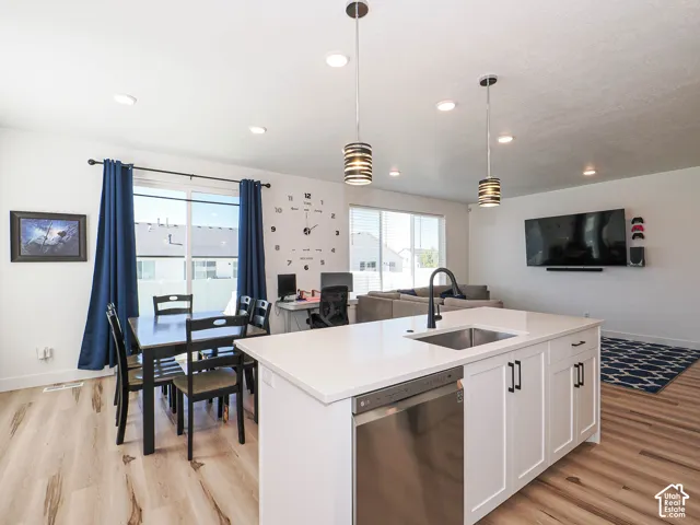 Open-concept living space with wood-finish flooring, white cabinetry, a kitchen island with a built-in sink, and stainless steel appliances