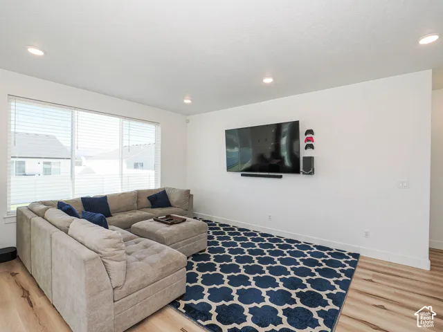 Recessed lighting illuminates the space, featuring a large window with blinds and wood-finish flooring