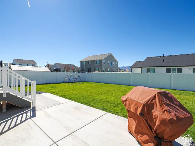 Expansive backyard featuring a lush lawn, concrete patio, and white vinyl fencing