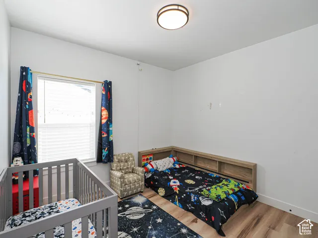 White walls, wood-finish flooring, a window with blinds, and an overhead flush-mount light fixture