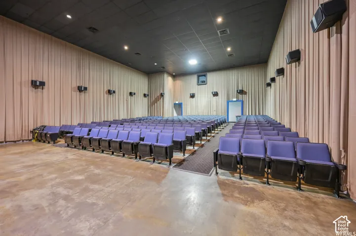 Spacious theater featuring tiered row seating, acoustically treated walls, concrete flooring, and ceiling-mounted light fixtures