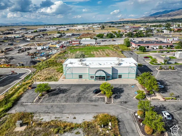 Commercial building with a prominent arched entrance, expansive paved parking lot, and mountain backdrop