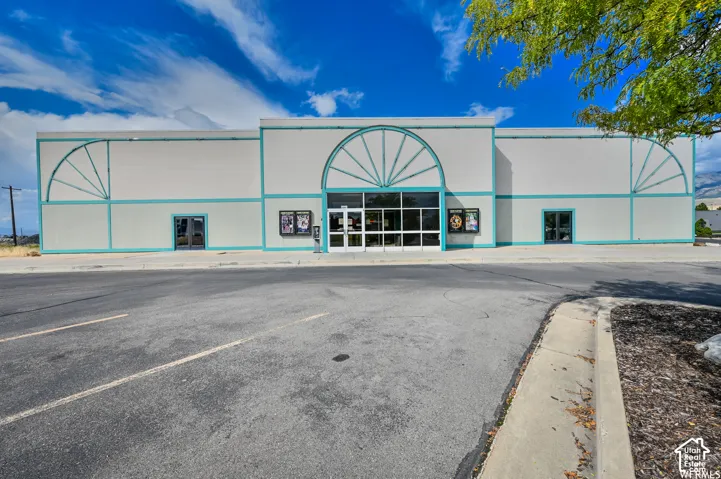 Commercial building featuring a white facade with teal accents, multiple entryways, an expansive paved parking area, and a landscaped perimeter