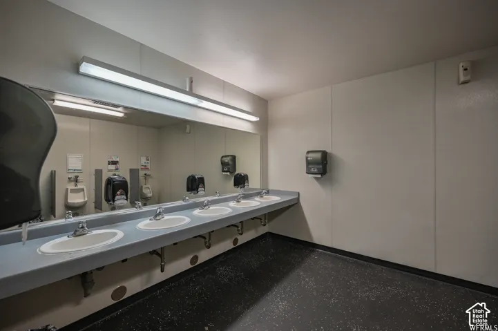 Multiple basin vanity with individual chrome faucets, large wall-mounted mirror, and overhead fluorescent lighting