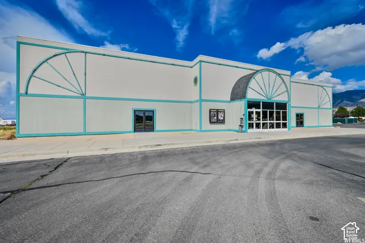 White facade with teal trim, arched entrance with glass doors, and decorative arched elements