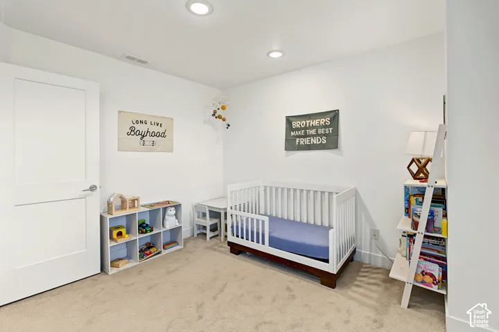 Recessed lighting, light beige carpeting, white walls, and a flat-panel interior door with brushed nickel hardware