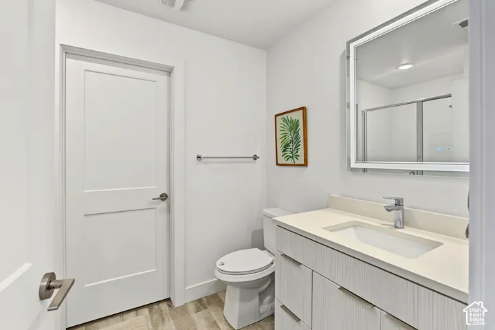 Wood-finish flooring, white vanity with integrated sink, chrome single-handle faucet, illuminated rectangular mirror, and glass-enclosed shower
