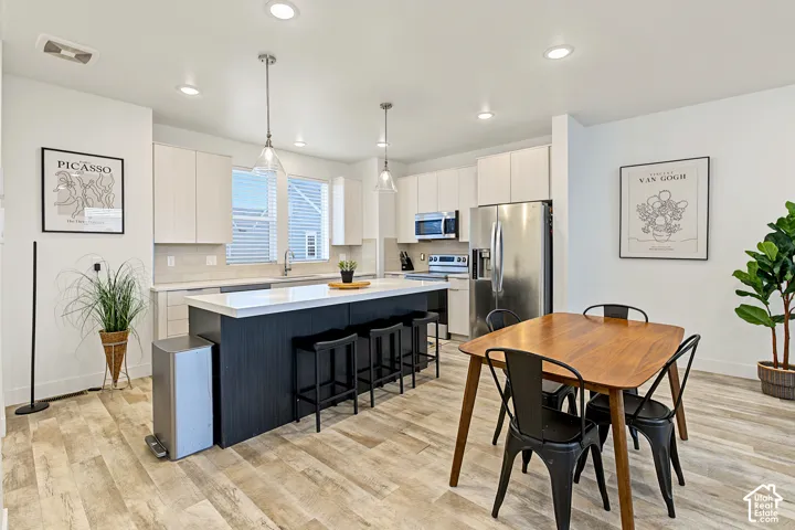 Open-concept kitchen with a large island, stainless steel appliances, light-toned cabinetry, and wood-finish flooring