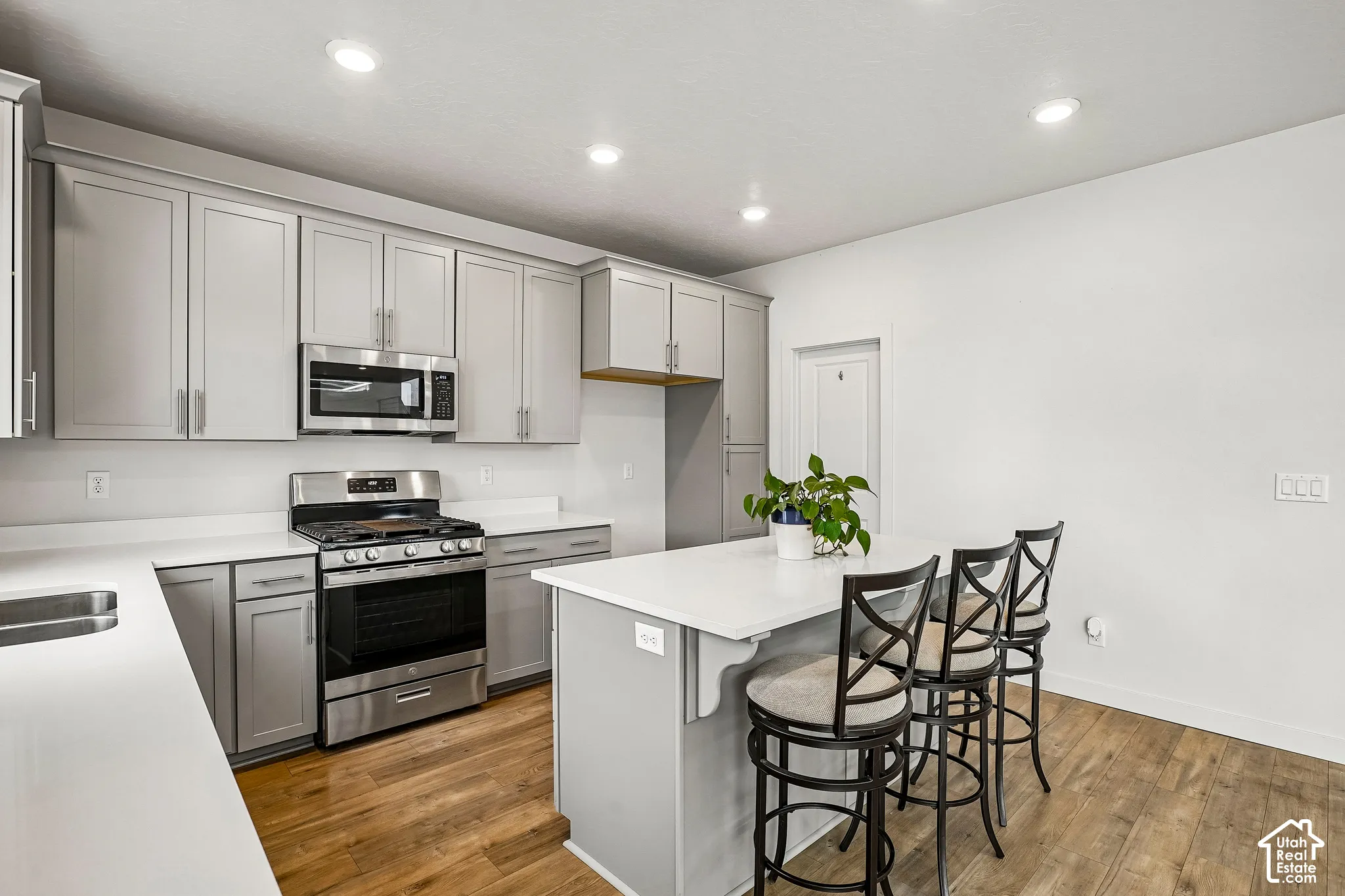 Light gray cabinetry, white countertops, stainless steel appliances, kitchen island, and wood-finish flooring