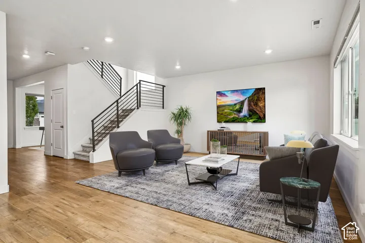 Open-concept living space with wood-finish flooring, recessed lighting, and a modern staircase featuring horizontal metal railings