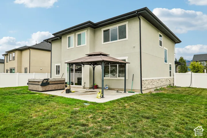 Expansive backyard featuring a manicured lawn, concrete patio, and built-in gazebo