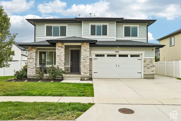 Two-story exterior with light blue siding, stone veneer accents, an attached two-car garage, concrete driveway, and a covered front porch