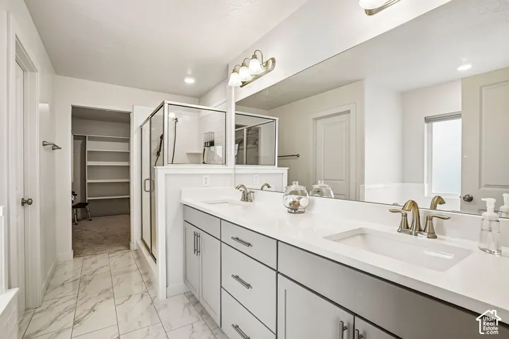 Primary bathroom featuring dual vanities with white quartz countertops, brushed gold faucetry, and ample storage cabinetry