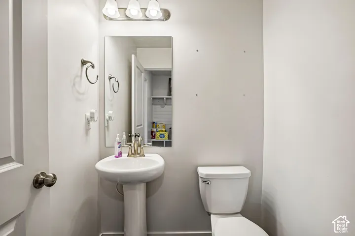 Pedestal sink with a polished brass-finish faucet, rectangular wall-mounted mirror, and three-light vanity fixture