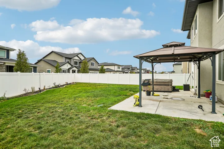 Expansive backyard featuring a manicured lawn, a white privacy fence, and a concrete patio with a gazebo