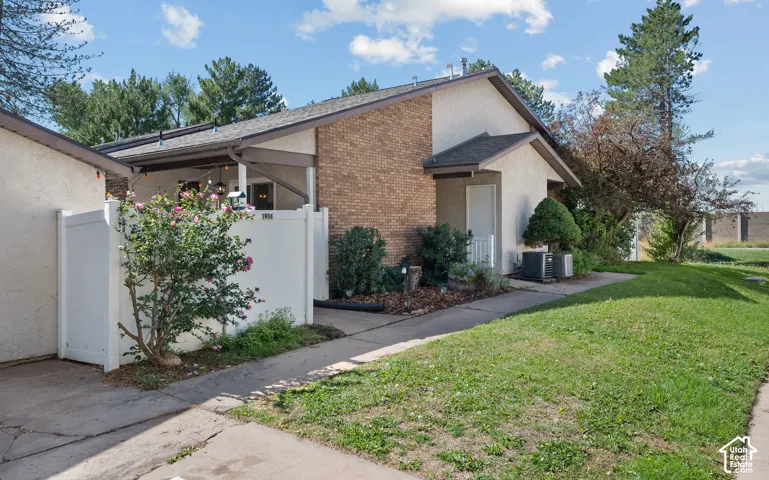 Brick exterior accent, stucco siding, covered entry, manicured shrubs, and a paved pathway