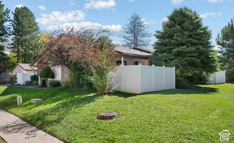 Manicured lawn with mature trees and shrubs, featuring a white vinyl fence and a concrete sidewalk