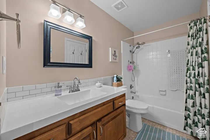 White subway tile backsplash, a single vanity with a white countertop and wood-finish cabinetry, and a shower-tub combination with white tile surround