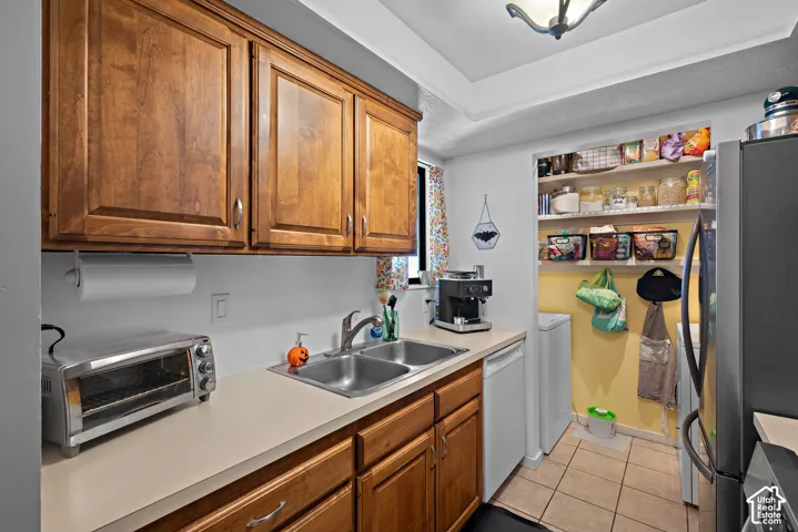 Wood-finish cabinetry, dual basin stainless steel sink, beige countertops, tile flooring, and a built-in pantry with shelving